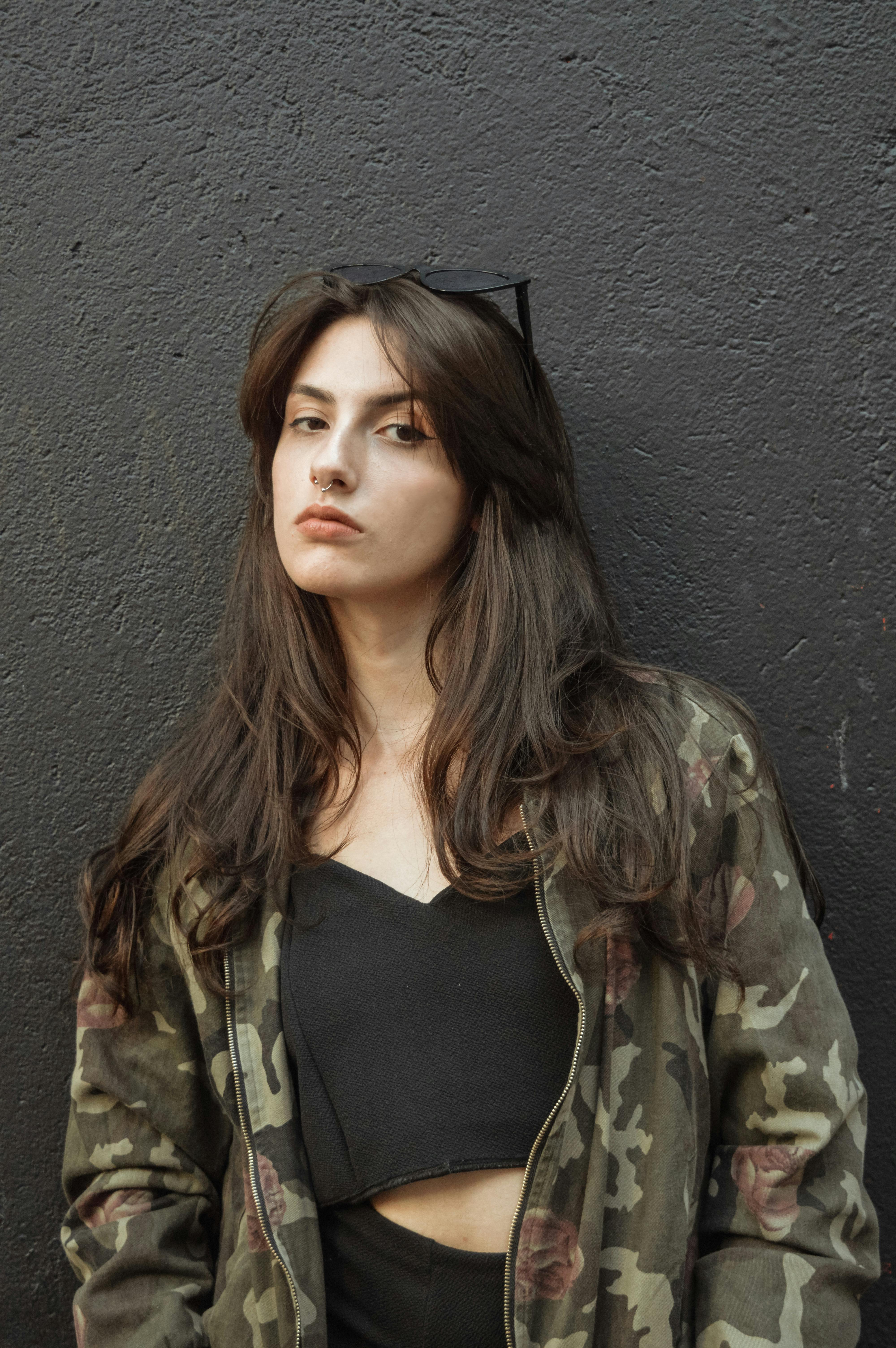 woman in black crop top and camouflage jacket standing against black wall