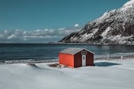 风景如画的白雪皑皑的沿海景观，拥有充满活力的红色小屋和引人注目的山脉