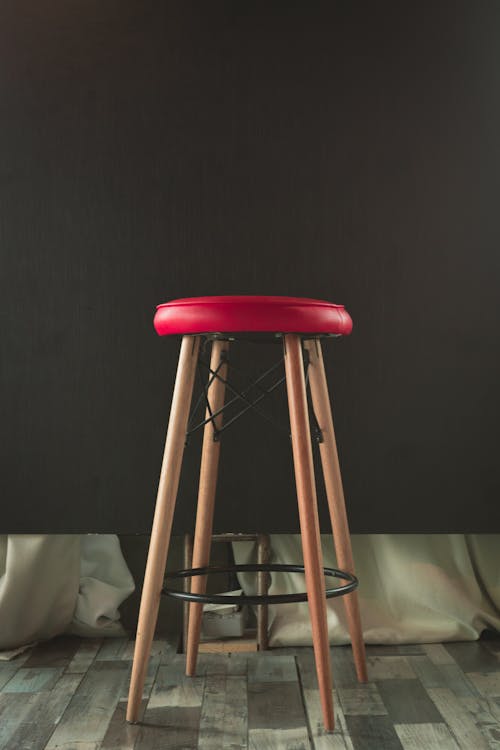 Free Stylish wooden stool with a red leather cushion against a dark background, perfect for modern interiors. Stock Photo