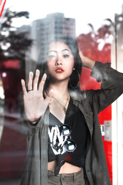 Portrait of a fashionable woman posing behind a glass window, showcasing modern style and elegance.
