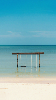 A tranquil beach scene with a swing over calm ocean waters, perfect for a serene vacation.