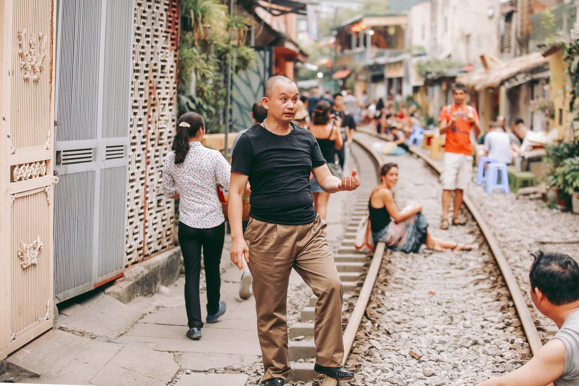 A vibrant urban street scene with people along a railway track, showcasing everyday life in a busy neighborhood.