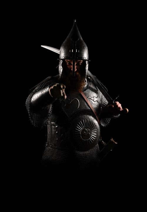 Free A medieval knight in full armor dramatically pointing forward, creating a powerful image against a dark background. Stock Photo