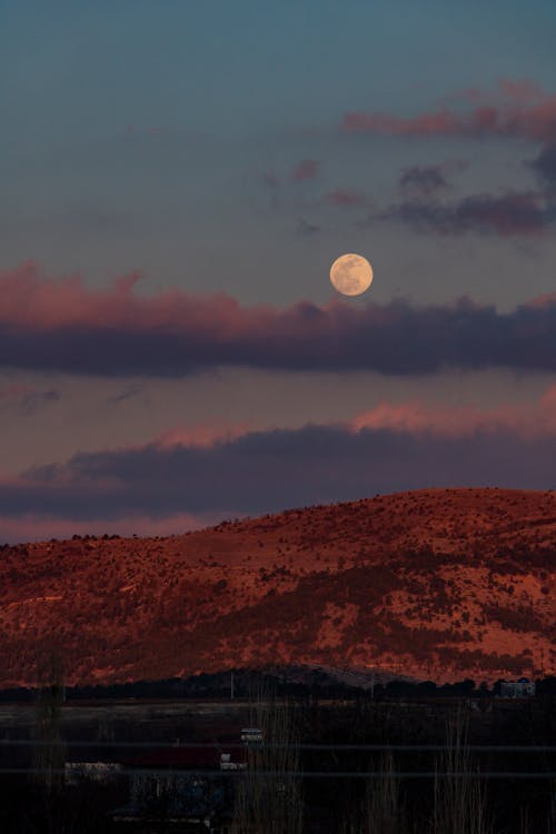The moon rises over a mountain range with a red sky