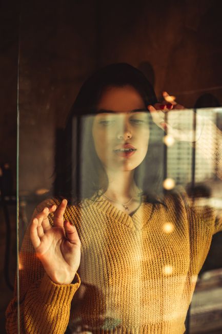 Stylish woman in a mustard sweater seen through glass with bokeh effect indoors.