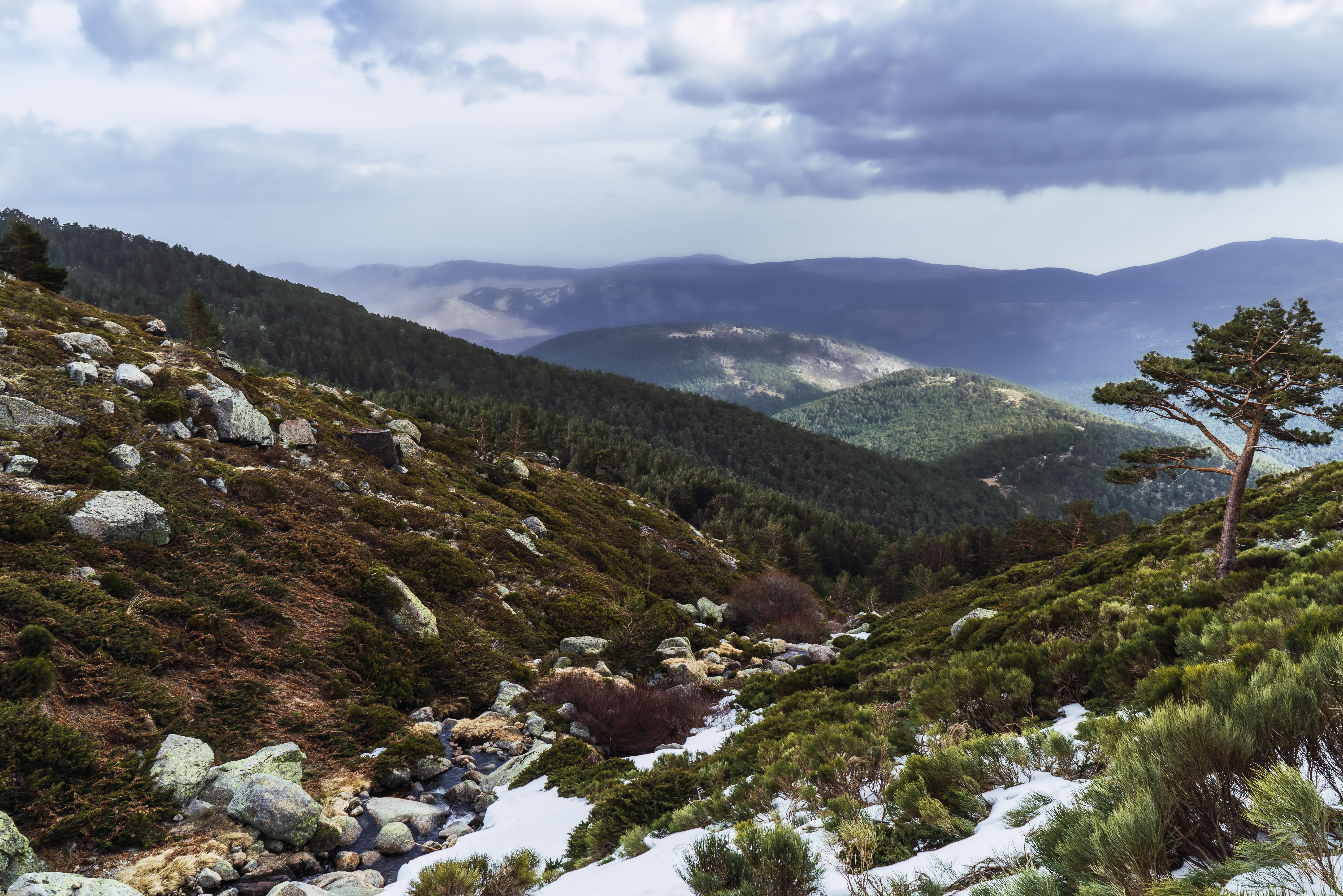 Beautiful winter view of Segovia mountains with snow, forests, and dramatic clouds.