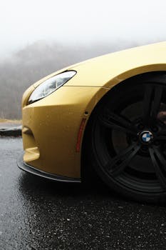 Dynamic shot of a yellow car driving on a wet road amidst dense fog, highlighting its sleek design.