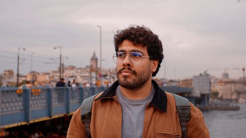 Free Man with eyeglasses and jacket stands on Galata Bridge, Istanbul with cityscape in the background. Stock Photo