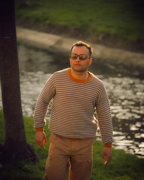 A man in a striped sweater and glasses standing by a river