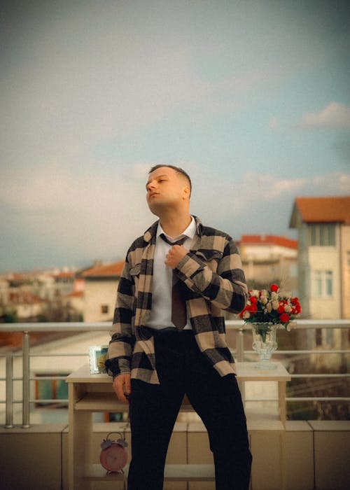A man in a plaid shirt and tie standing on a balcony
