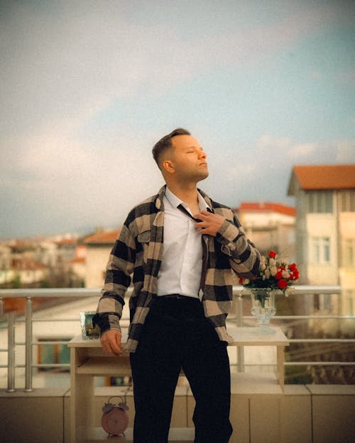A man in a plaid shirt and black pants standing on a balcony