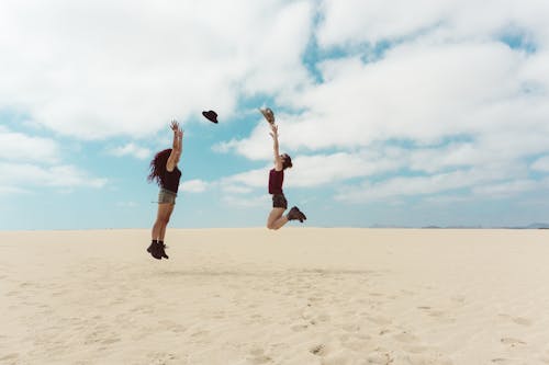 Two people jumping in the air on a sandy beach