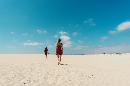 Two people walking on a sandy beach with a blue sky