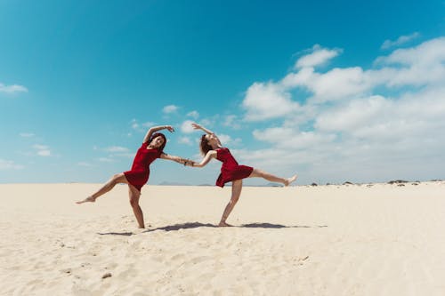 Two women in red dresses dancing on the beach