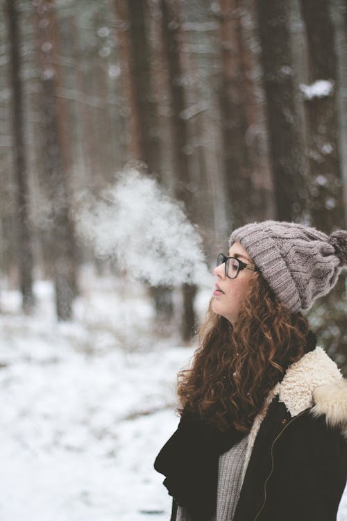 站立和在積雪覆蓋的森林上吸煙的女人