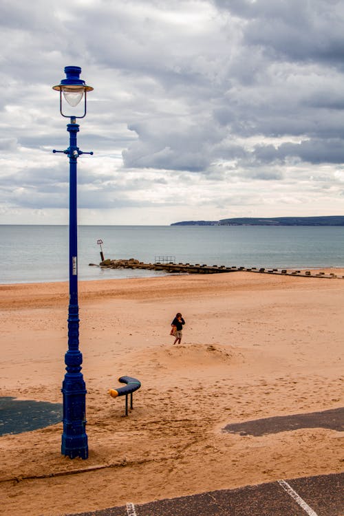 A person walking on the beach near a lamp post