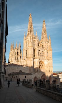 Burgos Cathedral, a Gothic landmark in Spain, captured during a vibrant sunset, showcasing its intricate architecture and urban setting.