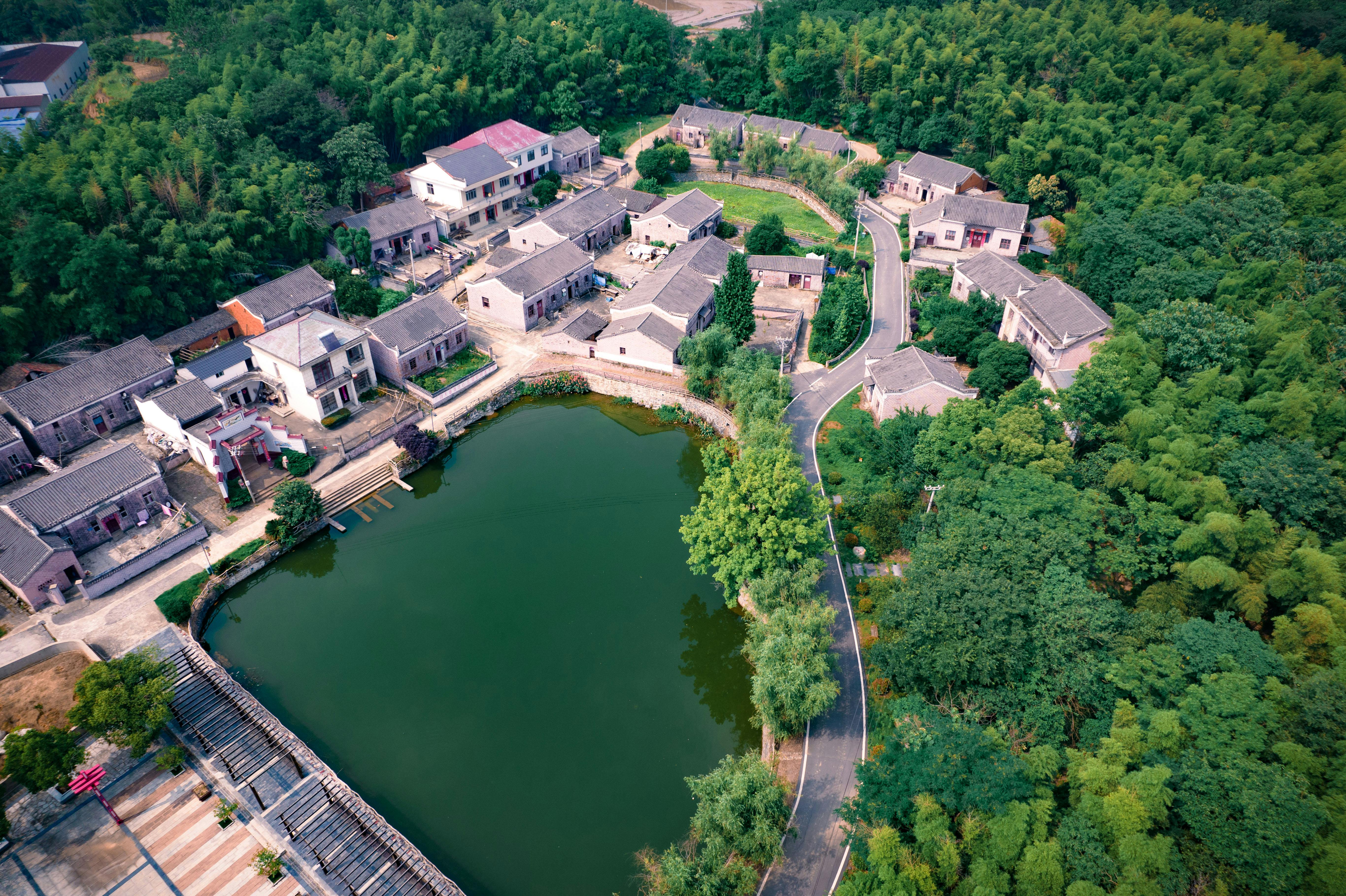 travel agent commission mayan tours - Scenic aerial shot of a traditional Chinese village surrounded by lush greenery and a tranquil pond.