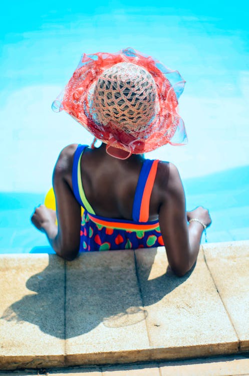 Foto de Mujer sentada en la piscina con sombrero y de espalda do Stock