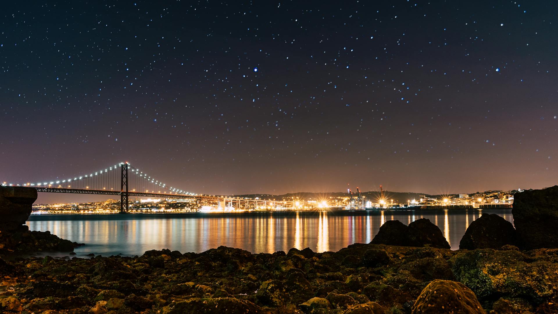 Captivating night scene of Lisbon with a starry sky above the illuminated suspension bridge.