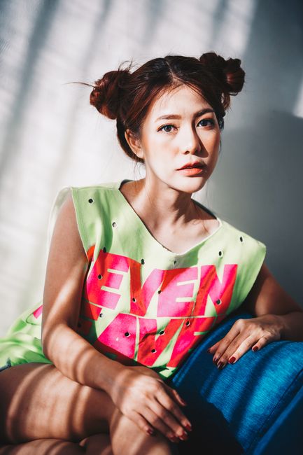 Stylish young woman poses with confidence in vibrant casual wear under sunlight indoors.