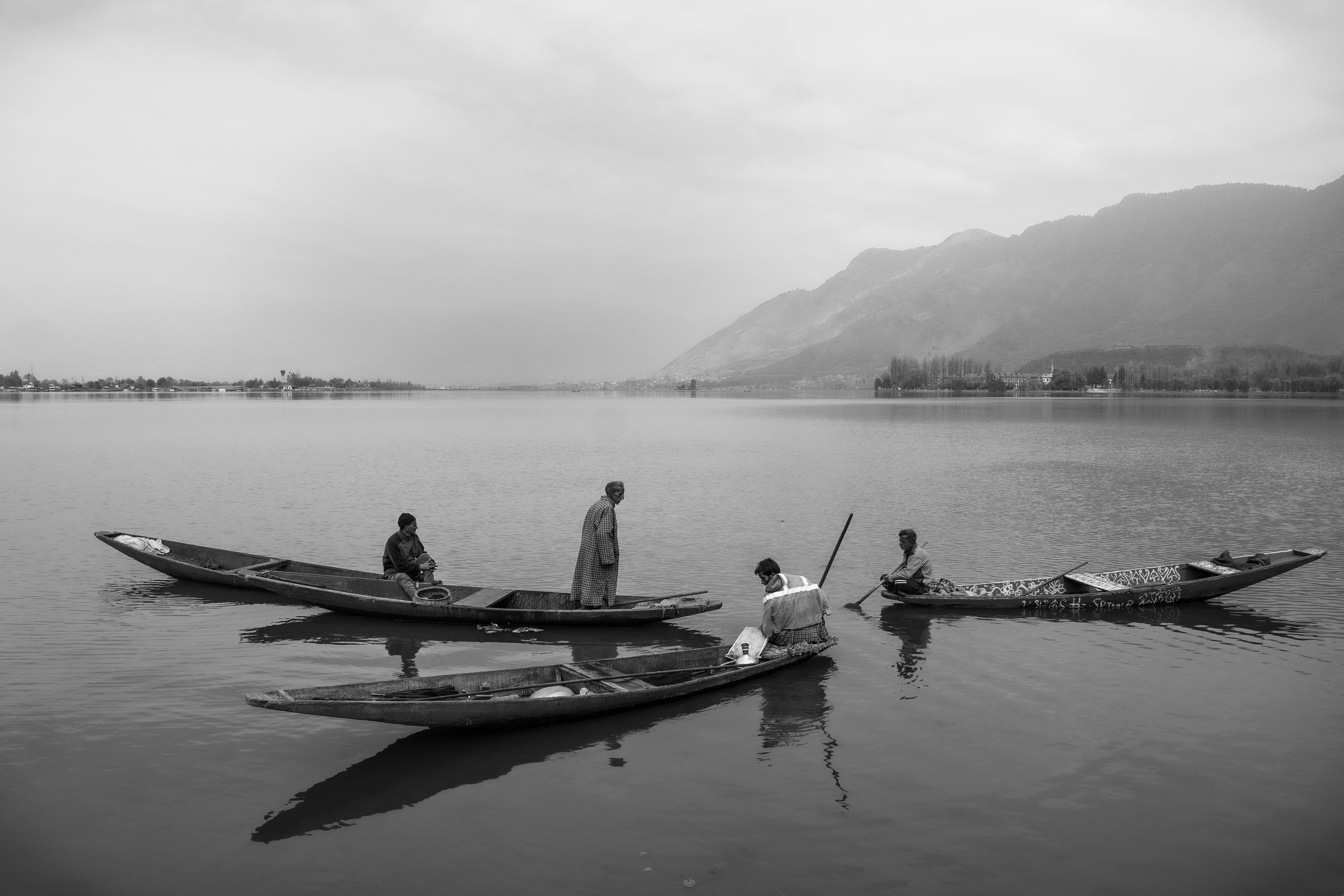 Black and white photo of fishermen in rowboats on Srinagar's Dal Lake, surrounded by hills.