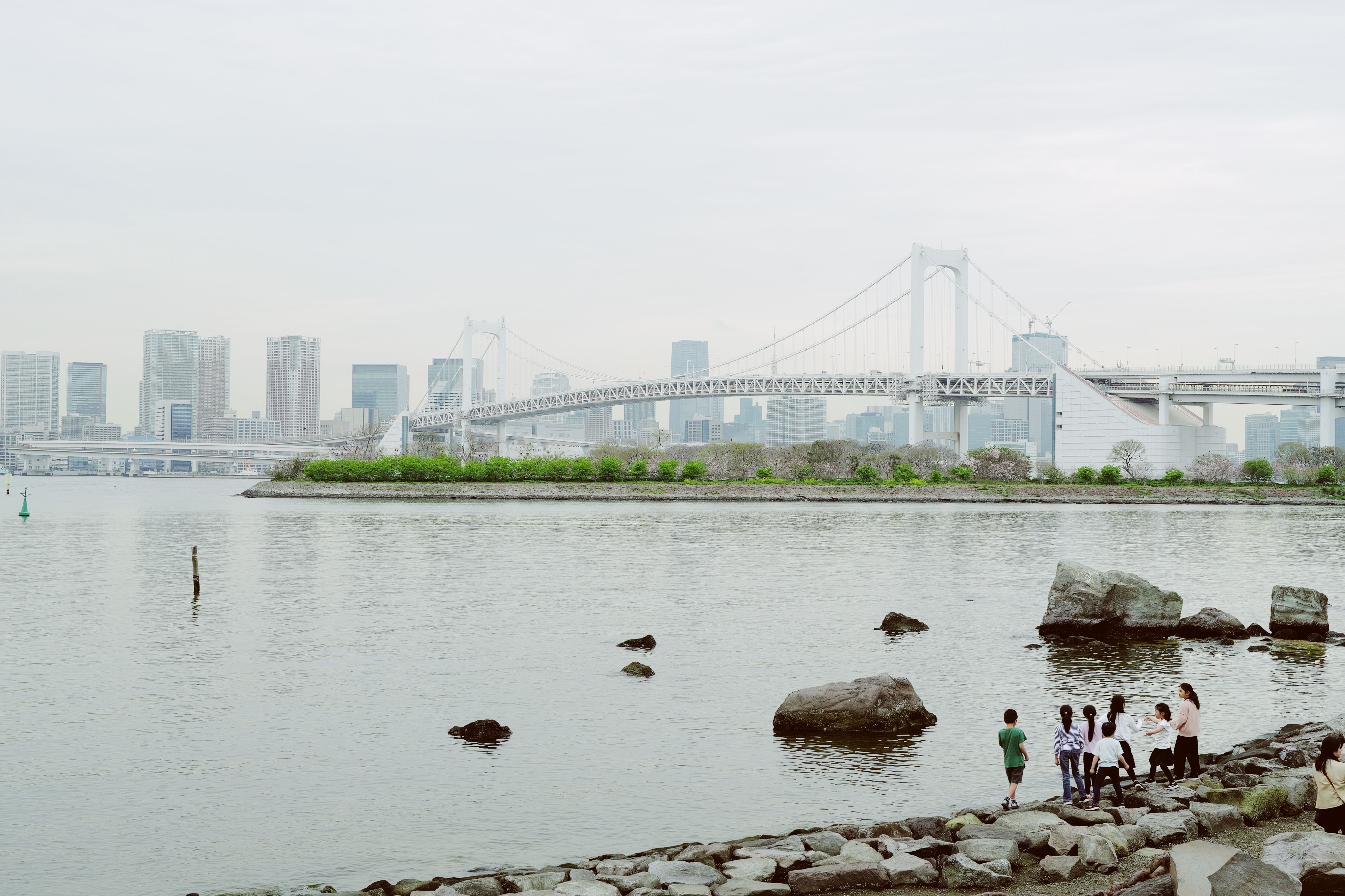 Children playing by the bay with a view of Tokyo's Rainbow Bridge and skyline