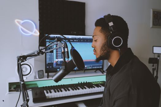 A musician recording vocals in a modern home studio setup with professional audio equipment.