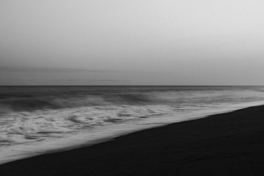 Serene black and white photo of a tranquil beach with soft waves and horizon.
