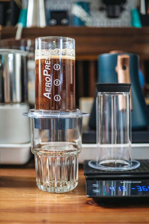 A glass of coffee sits on a counter next to a scale