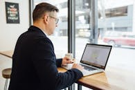 一名成年男性在咖啡馆里用笔记本电脑工作，喝着咖啡