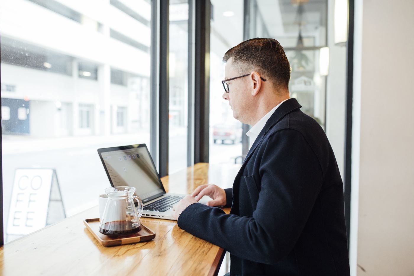 A person working on a laptop with a coffee beside a café window
