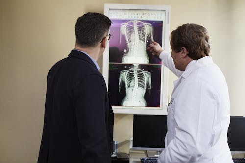 Doctor Pointing X-ray Result Beside Man Wearing Black Suit