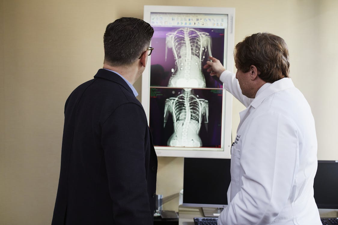 Doctor Pointing X-Ray Result Beside Man Wearing Black Suit