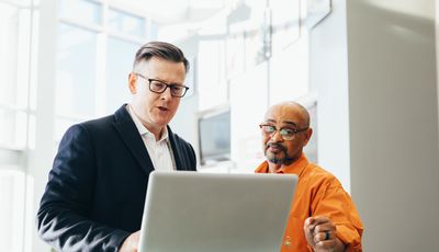 Free Two business professionals engaged in a collaborative discussion over a laptop in a modern office setting. Stock Photo