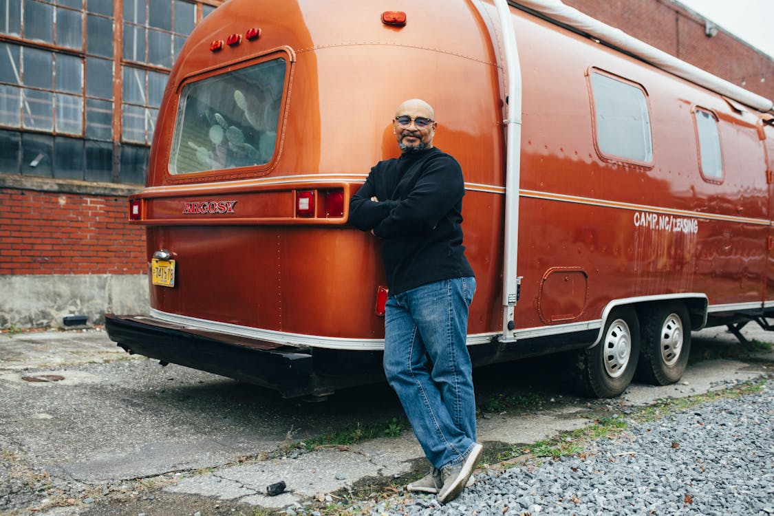 Man Standing Leaning on  Orange Camper