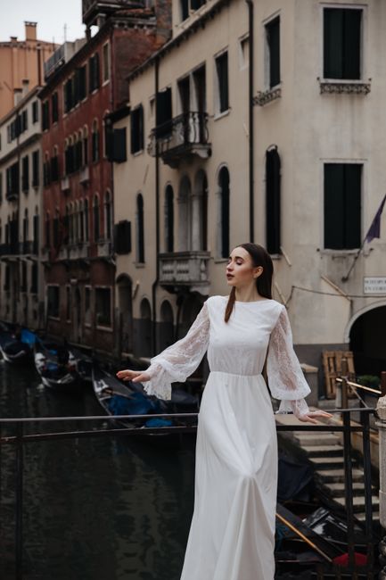 A stylish woman in a white dress posing elegantly by a Venetian canal, showcasing timeless fashion.