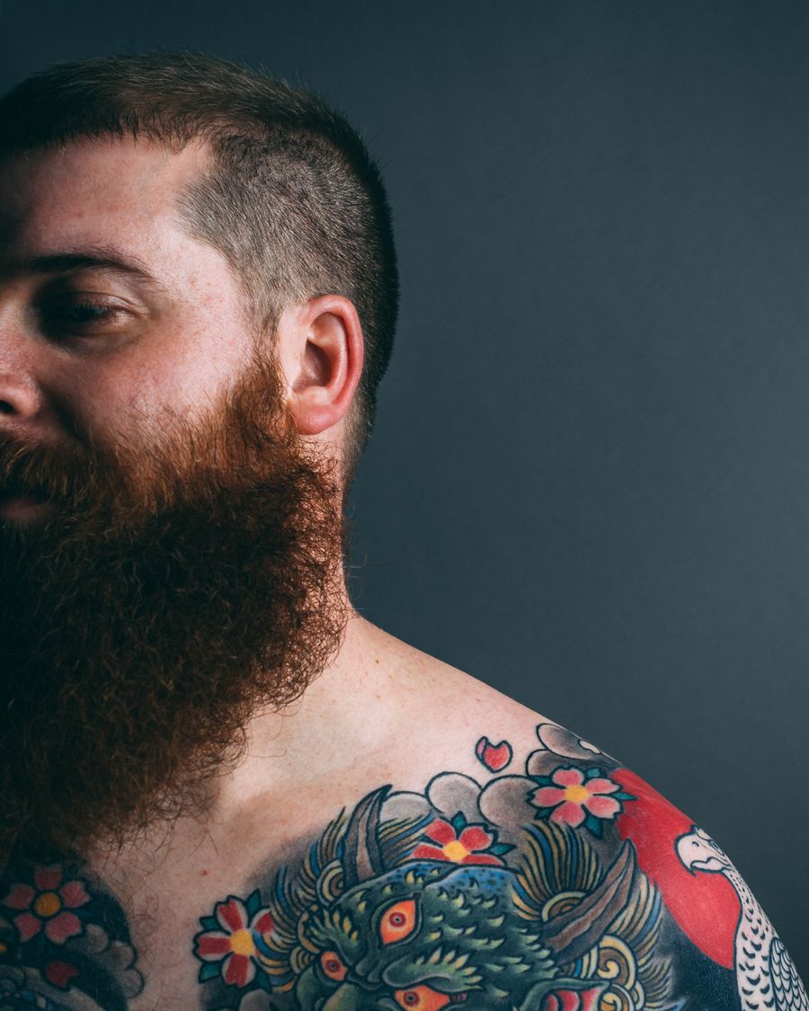 A portrait of a bearded tattoo artist showing his tattooed arm.