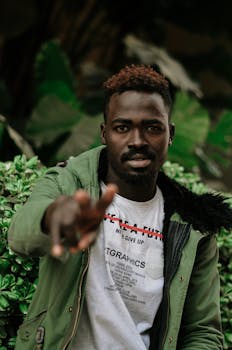 在郁郁葱葱的绿色背景前，一位时尚男子正指着相机拍摄肖像