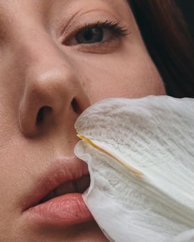 Close-up of a woman's face with a serene expression and a white flower petal near her lips.