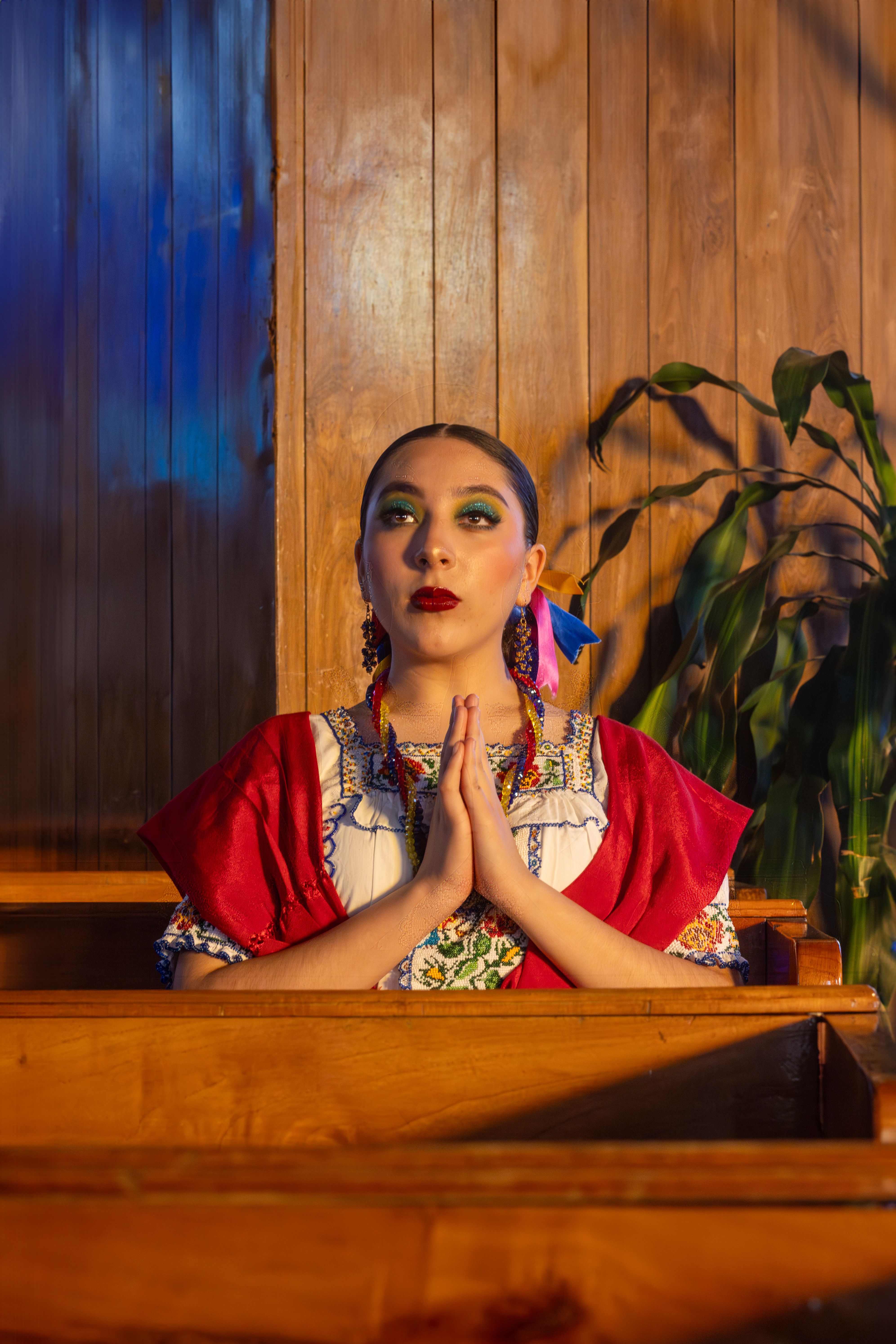 A Mexican woman in traditional attire praying in a wooden church interior, embracing cultural heritage.