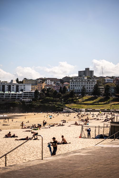 Free People enjoying Bondi Beach under clear skies with Sydney cityscape. Stock Photo