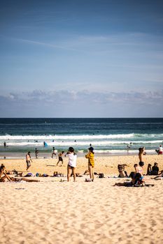 People enjoying a sunny day at Bondi Beach, Sydney with waves and clear skies.