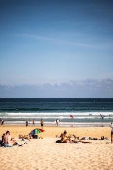 A lively scene at Bondi Beach with people sunbathing and swimming under clear skies.