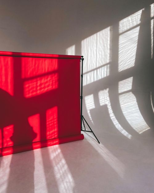 Free Artistic studio setup with red backdrop and dramatic sunlight creating reflections and shadows. Stock Photo