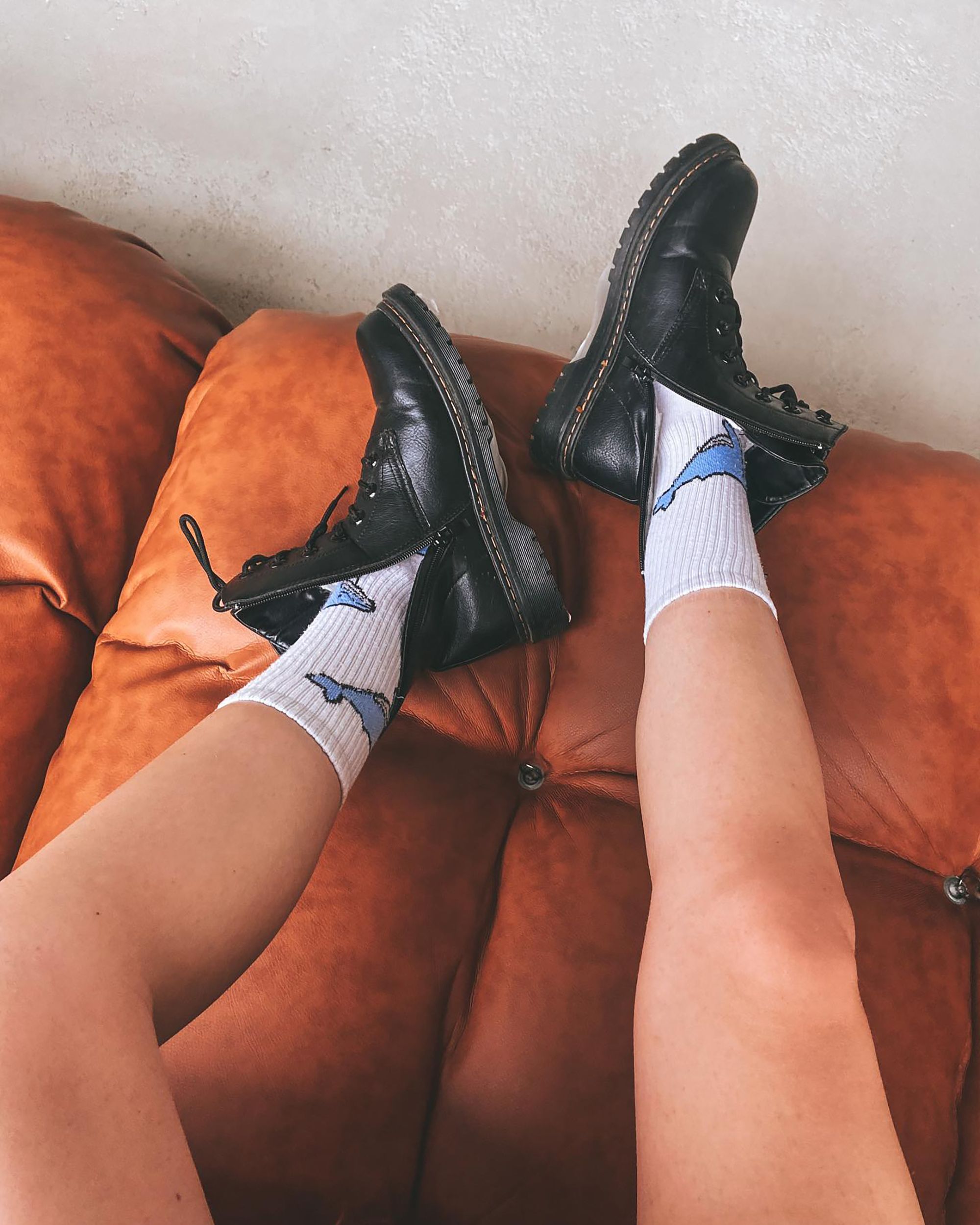 Casual shot of a woman in black boots and white socks on a stylish leather couch.