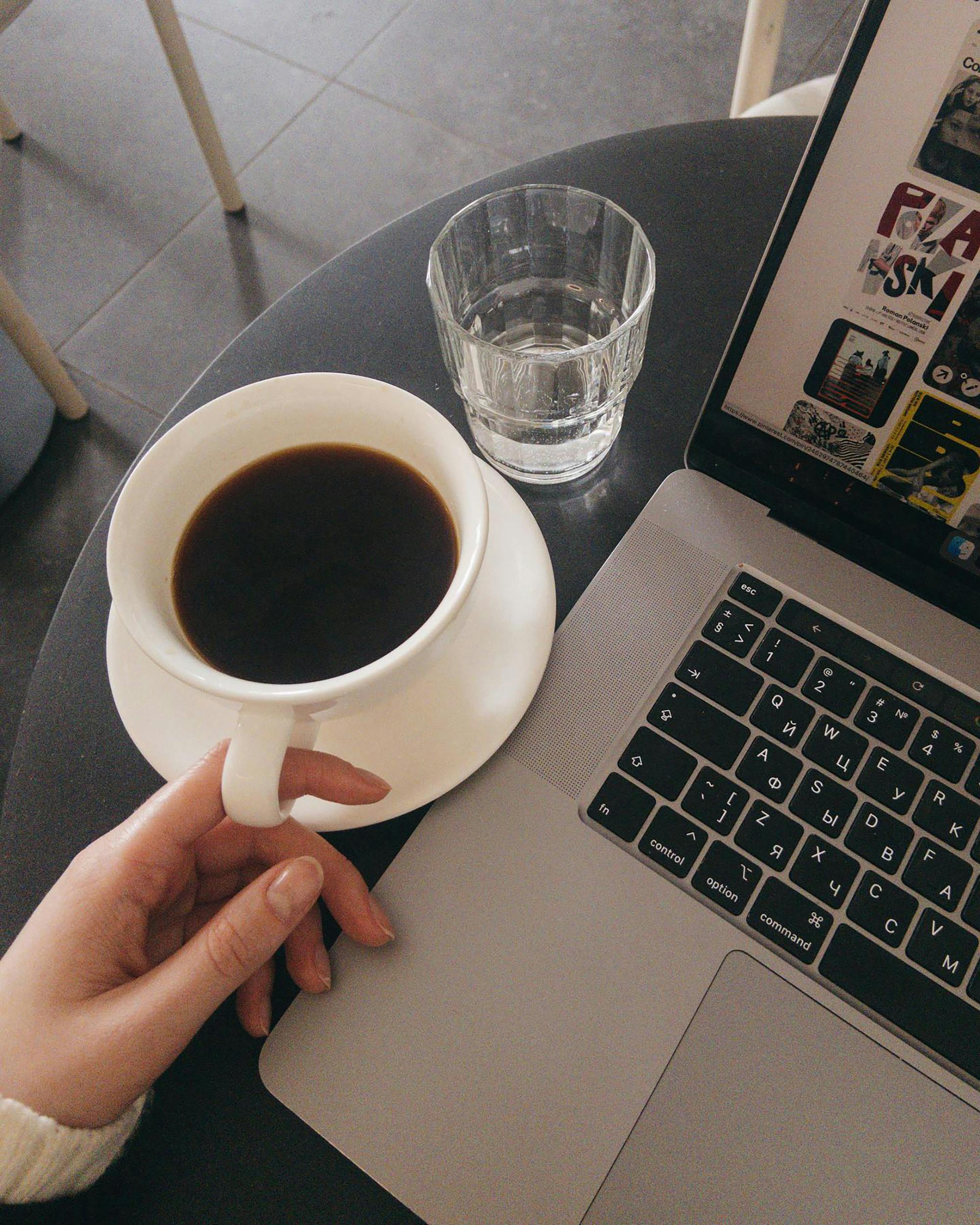 A cozy workspace featuring a laptop, coffee cup, and glass of water on a table.