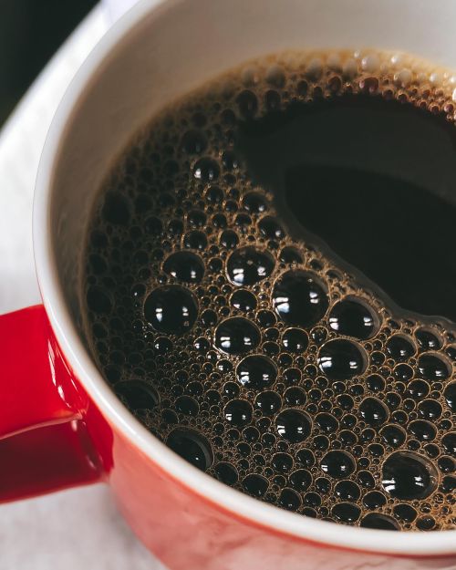 Free A fresh cup of coffee with bubbles in a red mug, perfect for caffeine lovers. Stock Photo