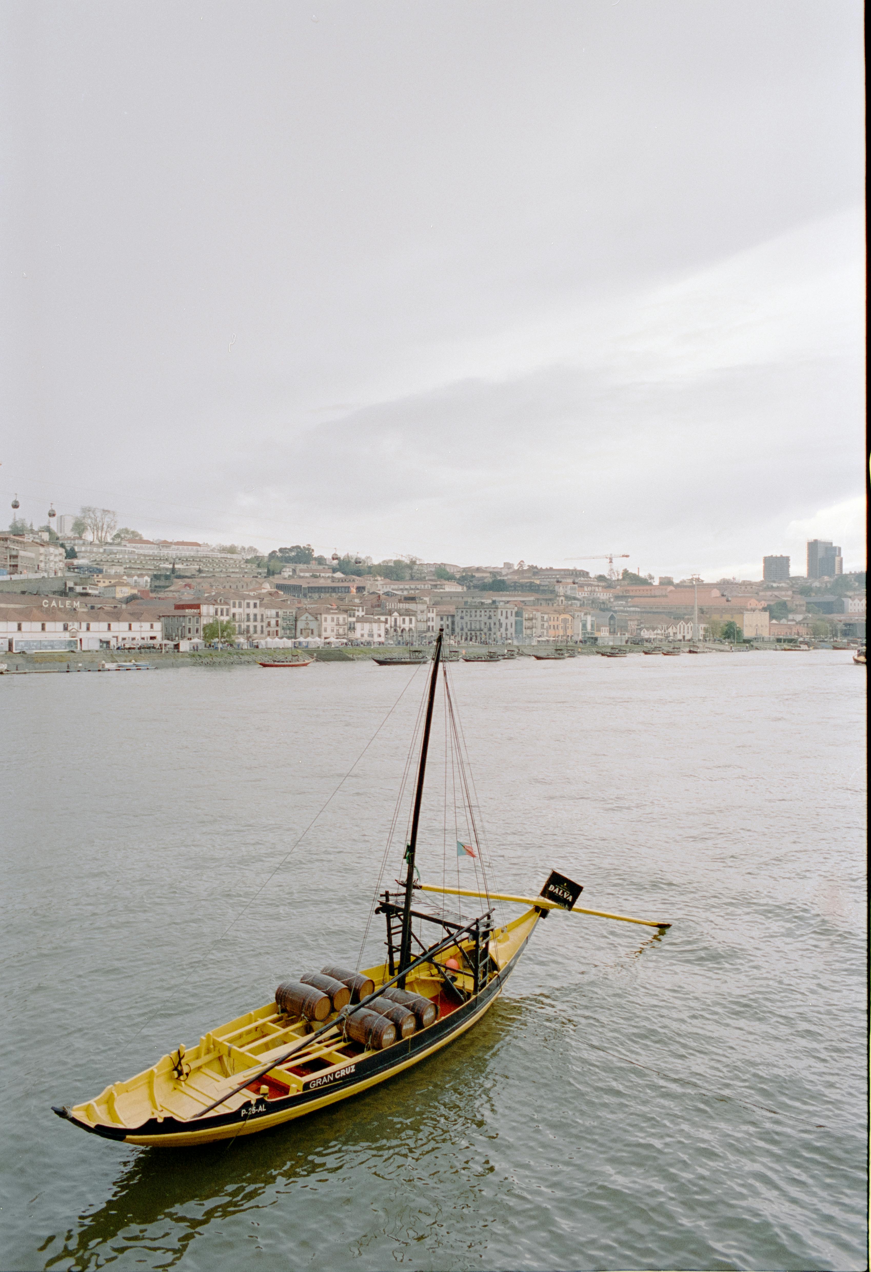 A traditional Portuguese boat sails on the Douro River with Porto cityscape in the background.