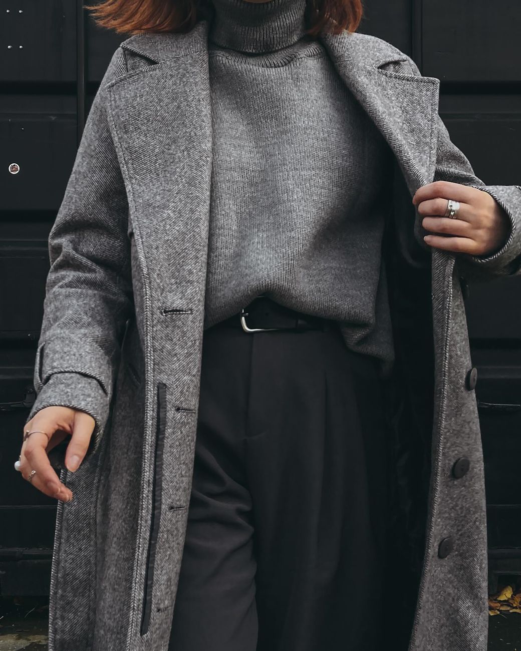 Fashionable woman wearing a gray coat and sweater, posing confidently.